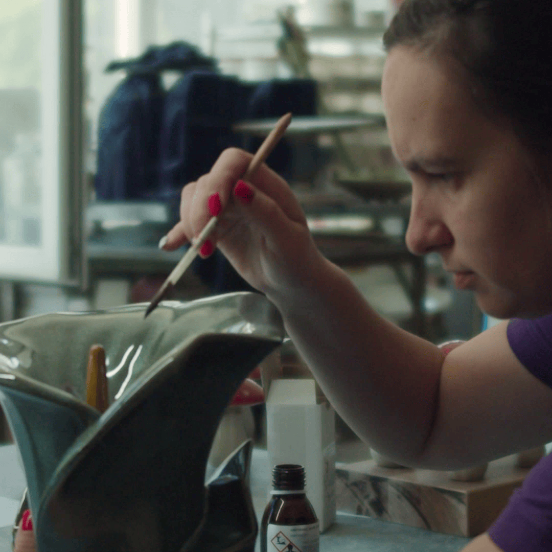 Person painting a ceramic object with a brush in a workshop setting