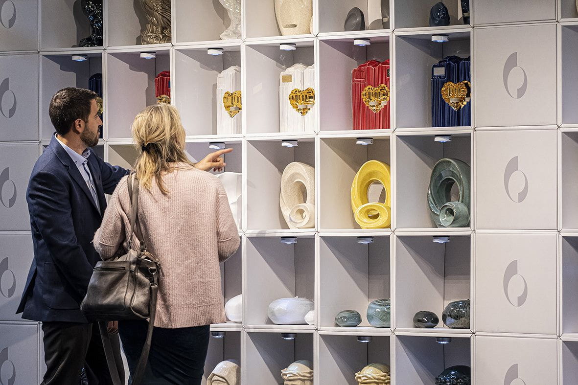 Two people looking at ceramic art urns in a display case. Pulvis Art Urns