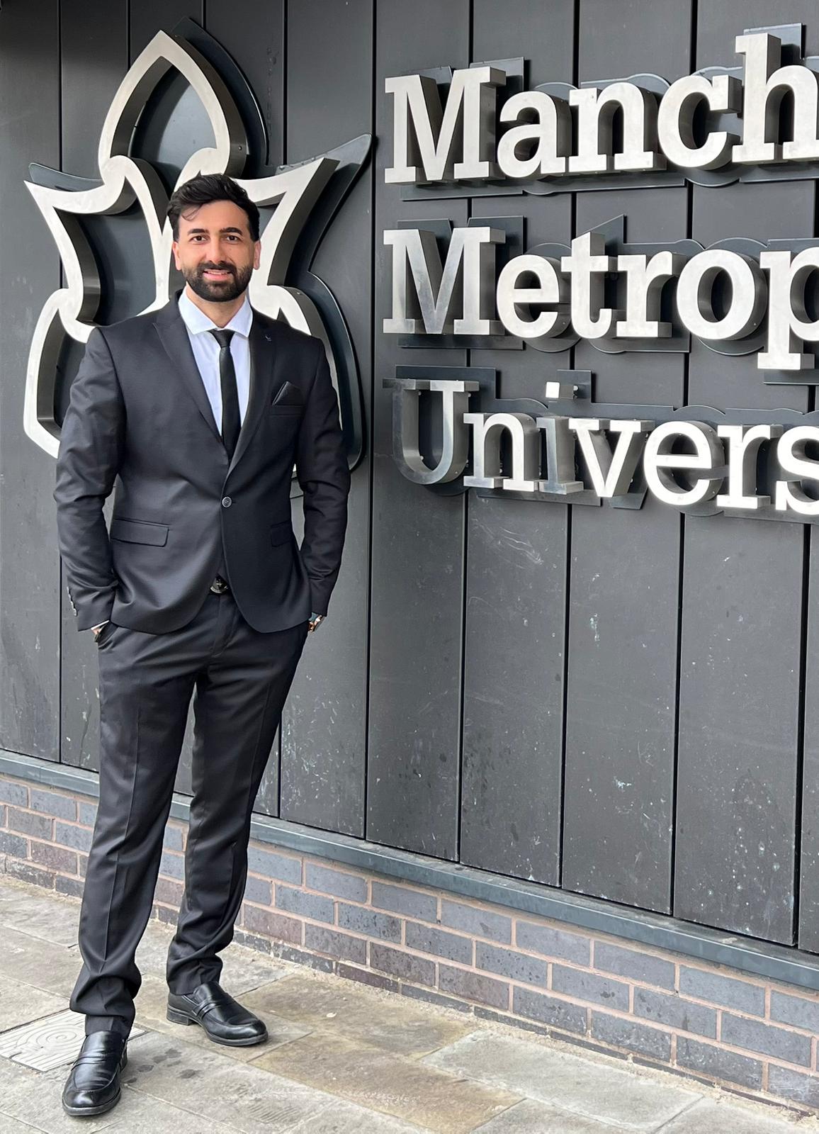 Man in a suit standing in front of Manchester Metropolitan University signage. Pulvis Art Urns - sales representative
